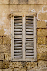 Fototapeta na wymiar Old wooden shutter in a house wall built of Malta stone blocks