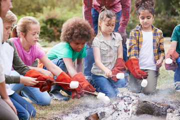 Team Leader With Group Of Children On Outdoor Activity Trip Toasting Marshmallows Over Camp Fire