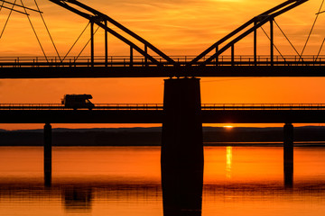 Fototapeta na wymiar Silhouette of vehicle on bridge over idyllic river
