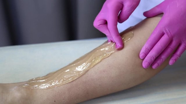 azulene depilation. wax hair removal, shugaring. concept of smooth skin without hair. azulene color. the master puts azulene on the girls legs