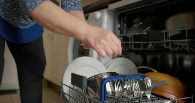 Mature woman emptying the clean dishwasher at home
