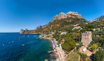 Aerial view of rocky beach, coastline of the village of Nerano. Private and wild beaches. Turquoise, blue surface of the water. Vacation and travel concept. Old tower and campsite for motorhomes