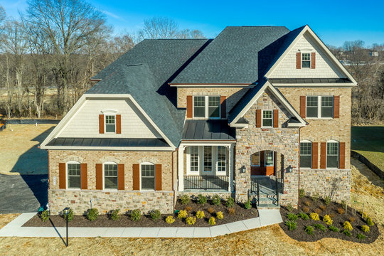 Aerial view of luxury single family mansion home covered w/ shingle, brick, stone, double peak gable, gambrel, asphalt shingle roof, decorative arch double hung sash windows w/ matching dark shutters