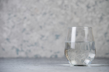 A glass of water on a gray concrete background. Vertical photo.