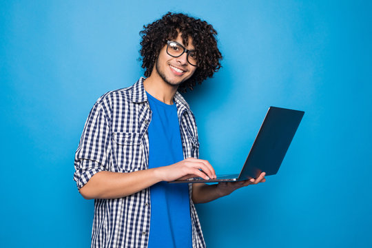 Young Curly Handsome Man With Laptop Isolated On Blue Background