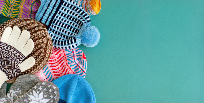 Warm clothes in the form of hats, gloves, mittens on a turquoise background. A panorama of hats, mittens, gloves for the cold seasons. Knitted clothes of different types and colors.