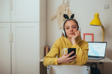 young teenage girl sitting in her room using mobile phone listening music