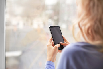 Young woman with mobile phone near window