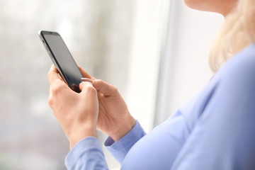 Young woman with mobile phone near window