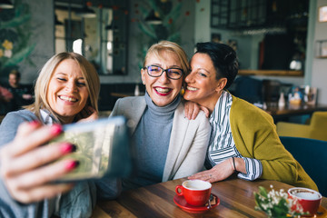 woman friends on coffee break at cafe, using smartphone for taking picture