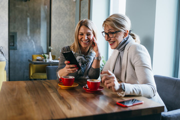 women on coffee break at cafeteria using mobile phone