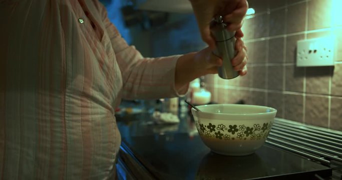 Mature woman mixing eggs by the stove and seasoning with pepper
