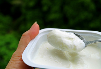 Closeup a bowl of yogurt in hand and scooping with spoon
