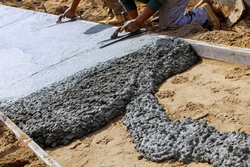 Construction workers laying concrete mixer with concrete mixer on sidewalk