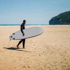 Young surfer with board and neoprene suit at the beach