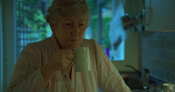 Mature woman drinking coffee by the stove in kitchen