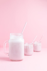 Set of three strawberry milkshakes with jug on a pastel pink background. Healthy food