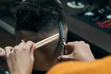 Hairdresser cuts the nape of a curly-haired young man with hair scissors. A white hairbrush in his hands.