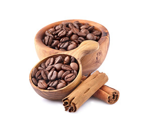 Coffee beans in a wooden spoon with cinnamon on white background.