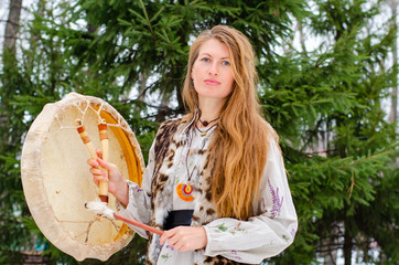 a woman in traditional clothing holds a shaman's drum, a white leather drum and wooden stick,...