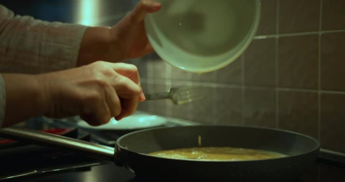 Close up on hands pouring egg into frying pan