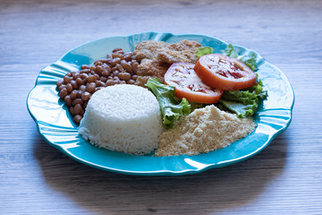Brazilian food dish. Beans, rice, salad, breaded fish and flour.