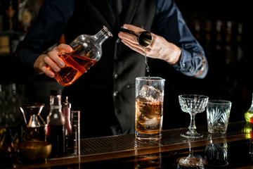Barman pouring required ingredient for cocktail from bottle with brown alcohol drink.