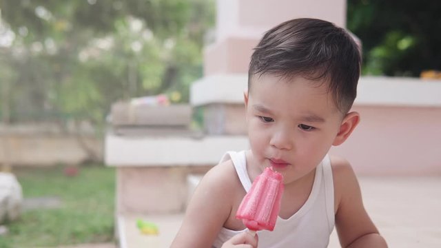 Slow motion Shallow depth of field video of a cute Asian boy eating a strawberry red  popsicle ice cream In his house backyard