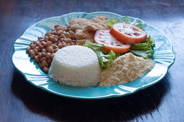 Brazilian food dish. Beans, rice, salad, breaded fish and flour.