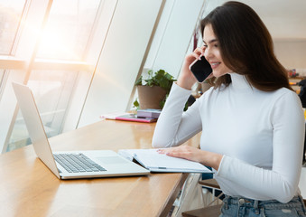 young beautiful businesswoman works in her laptop and speaks on the phone while sitting in the cafe...