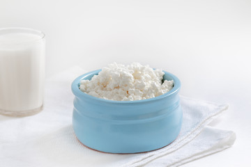 homemade fresh cottage cheese in a blue bowl on a white background, a glass of milk in the background, a napkin