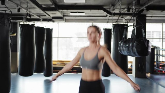 Tilt up three quarter angle view of fit determined young woman in crop top and leggings jumping rope among boxing bags in gym