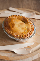 Savoury meat or steak pie in a foil tray with wooden cutlery