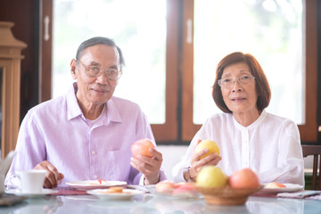 Asian elderly couple eating fruits and talking at home. Happy retirement lifestyle concept