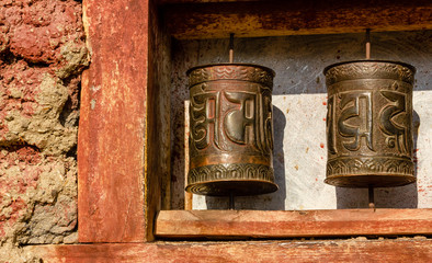 Obraz premium Prayer wheels with tibetan mantras on a red wall inside the ancient Buddhist monastery in the Himalayan village of Nako in Kinnaur, India. Tibetan text says, 