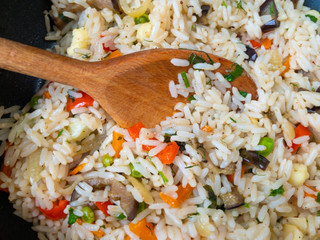 Top view on wooden spoon stuck in white rice cooked with vegetables.