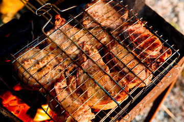 Large chunks of pork are fried on a grill over an open fire.
