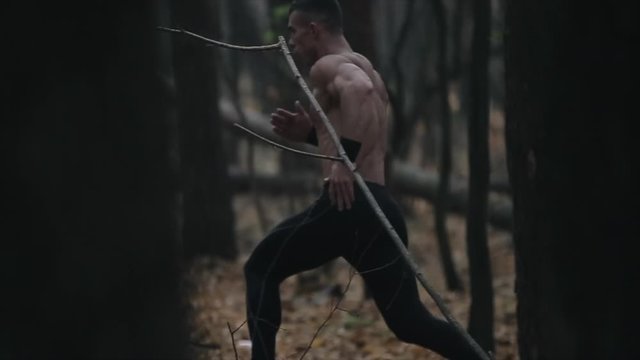 young muscular runner runs in the forest. Running between the trees. Slow motion