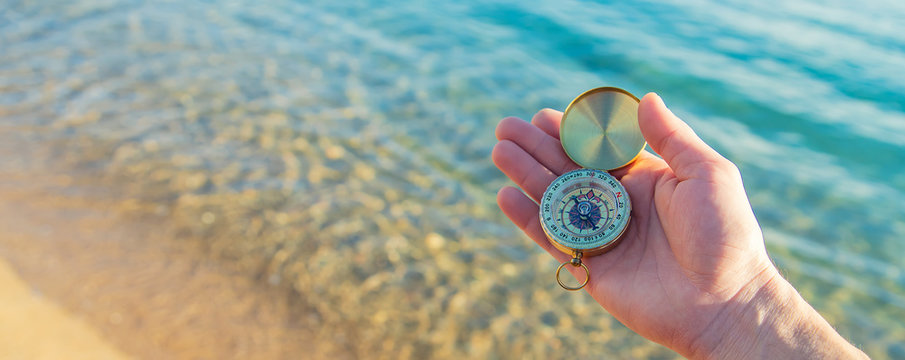 A man with a compass in his hands near the sea. Selective focus.