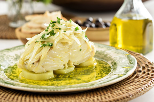 Table set for a dinner, with green decorated portuguese plate, glass of wine and some side dishes. A codfish with potatoes, onion and parsley is being served, an typical portuguese dish.