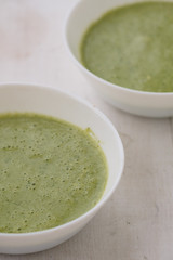 Spring detox broccoli green cream soup in white plates, bowl with crackers and stylish black cutlery on grey background. 