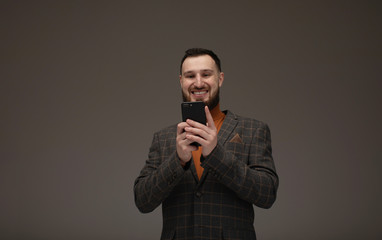 Handsome bearded model is posing with phone in hands over grey background.