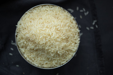 A scattering of rice, a handful of rice, rice in a metal bowl on a dark background. 