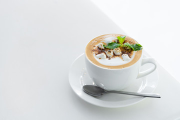 Close-up of Butterscotch latte coffee with marshmallow in a white cup and saucer on white table background.