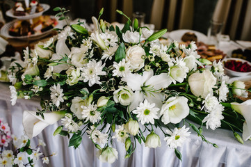 A composition of flowers and green is on a festive table at the wedding banquet hall. Close up.