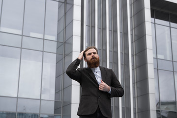 Portrait of an handsome businessman wearing jacket over office building in financial district outdoors. Young bearded Businessman outdoor. Successful entrepreneur dressed in formal wear.