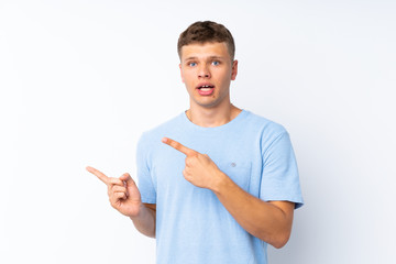 Young handsome man over isolated white background frightened and pointing to the side