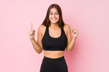 Young caucasian fitness woman doing sport isolated indicates with both fore fingers up showing a blank space.