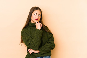 Young caucasian woman isolated en beige background looking sideways with doubtful and skeptical expression.