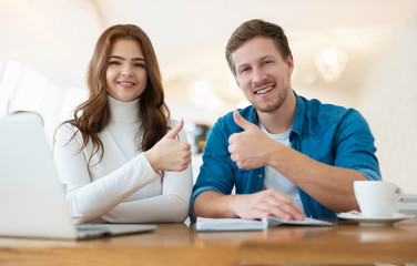 Fototapeta premium two young successful colleagues brunette woman and handsome man looking satisfied, working in laptop during coffee break both showing like signs, body language concept